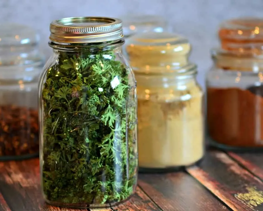 Mason jar filled with dehydrated parsley, and spice jars in the background