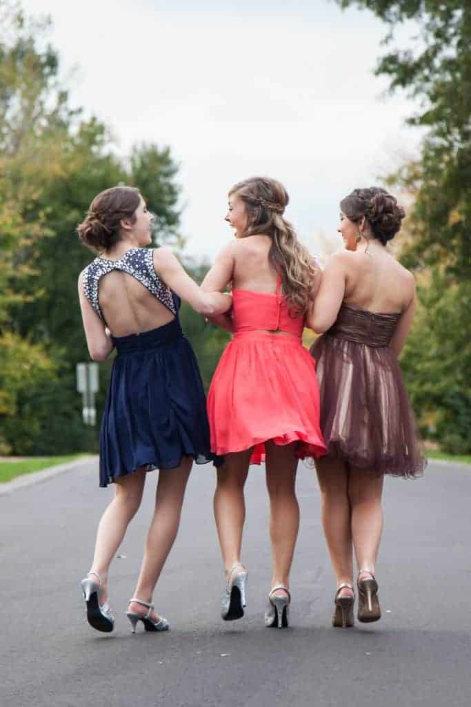 Three girls in prom dresses walking down a road chatting and laughing