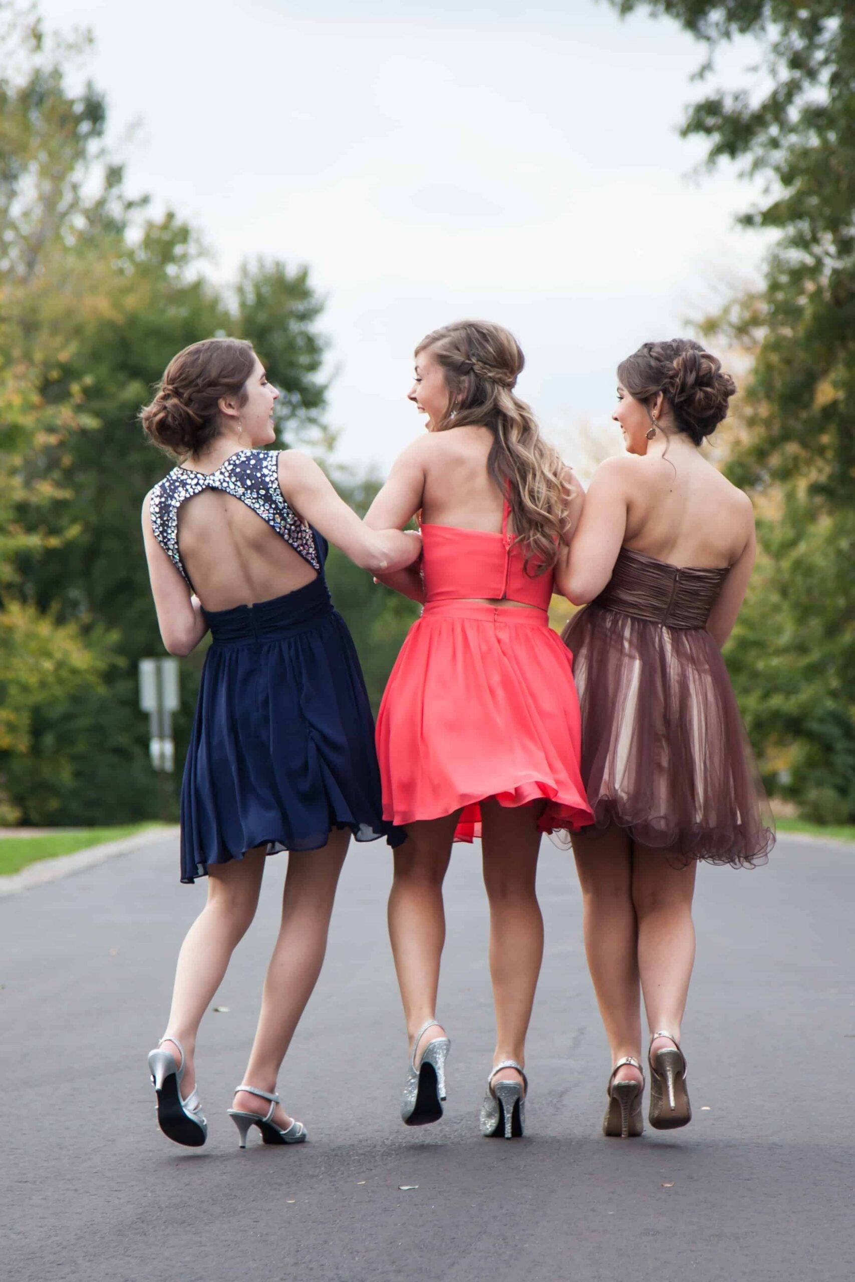 Three girls in prom dresses walking down a road chatting and laughing