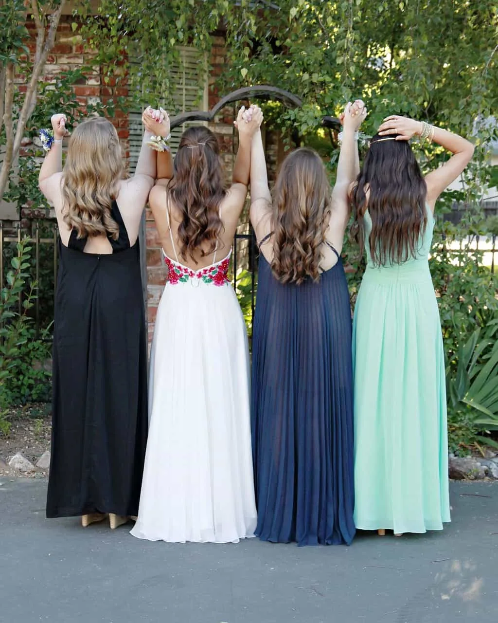 4 girls in prom gowns facing away from camera holding hands