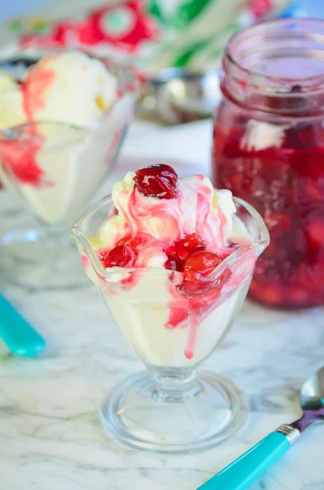 vanilla ice cream topped with cherry sauce in a sundae dish with a jar of cherry sauce in the background. 