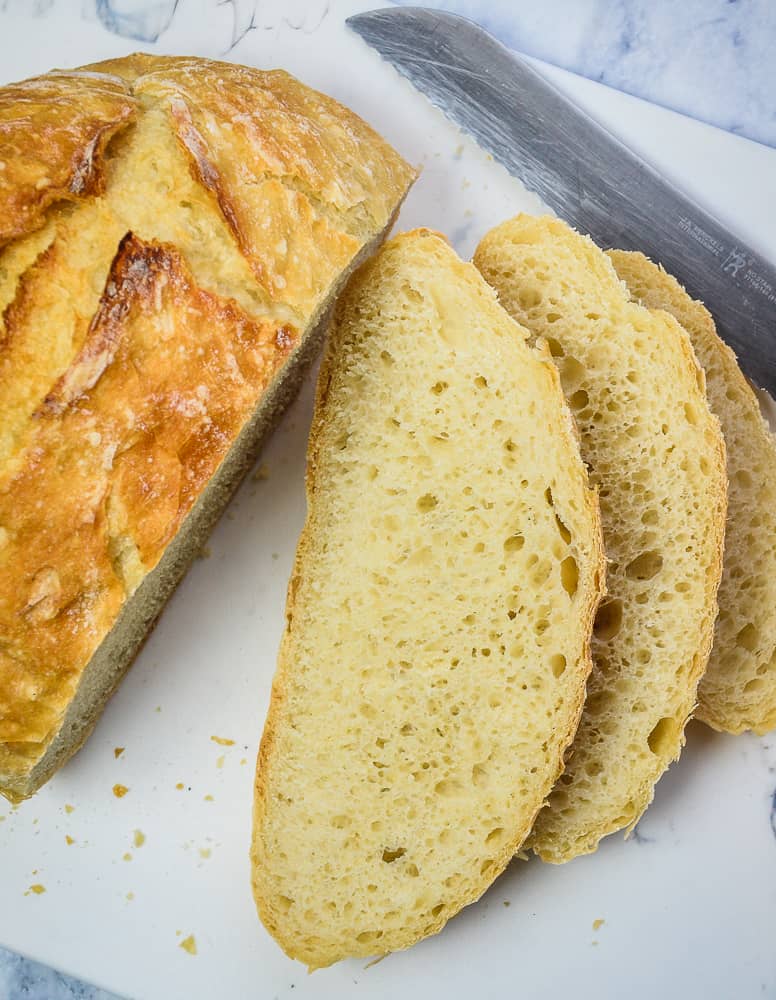 Sliced Crusty No Knead bread on a cutting board with bread knife.