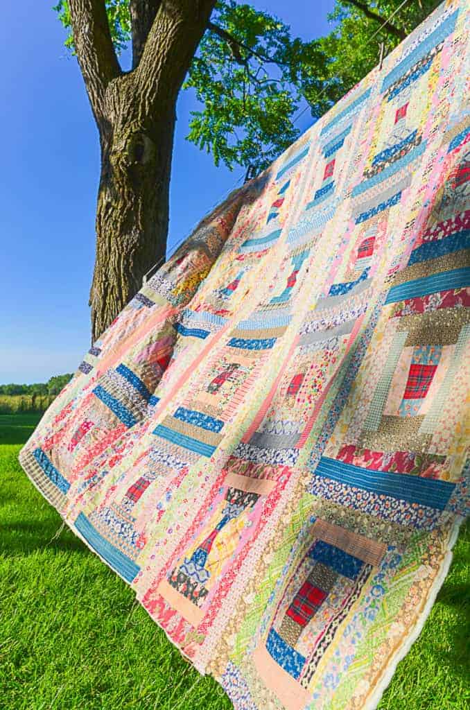  A log cabin quilt hanging outdoors of a clothesline with blue skies in the background, the quilt top is made from vintage feedsack fabric. 