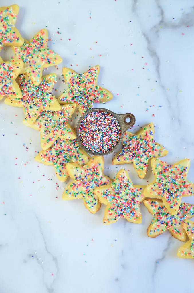 Orange Confetti Shortbread cookies on a marble counter top, with a small measuring cup of non-peril candies. 