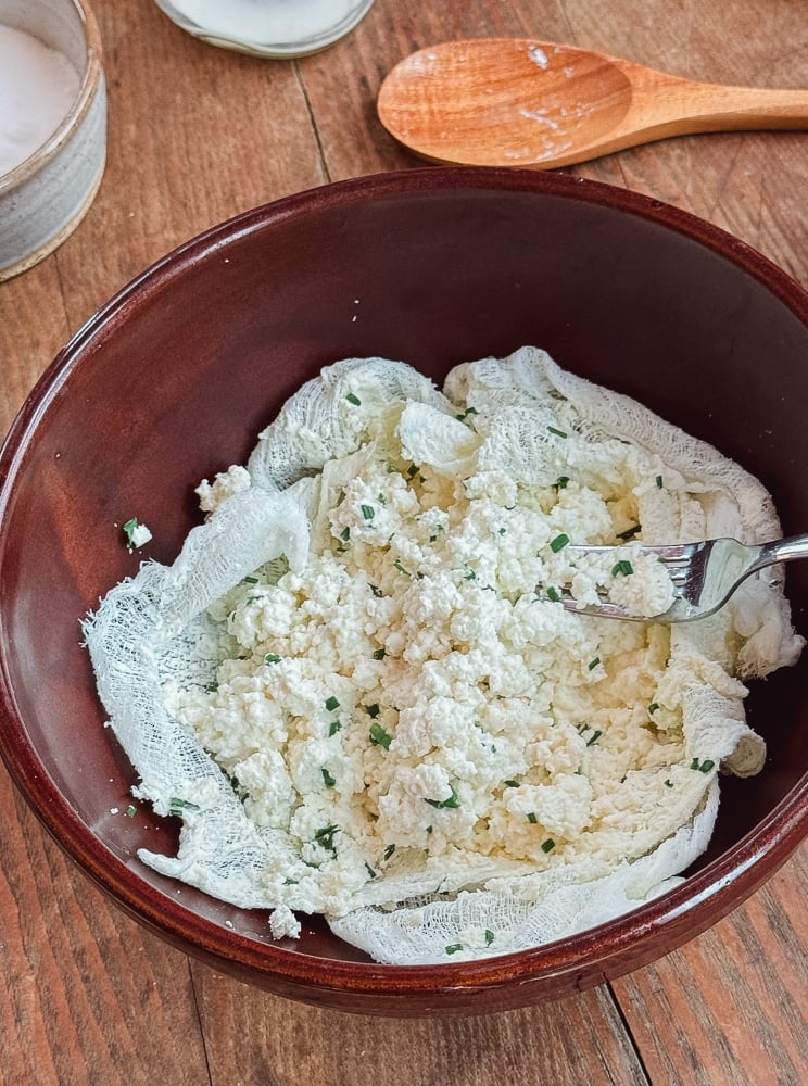 Fresh farmers cheese curds with chopped chives in a brown pottery bowl ready to press into a mold