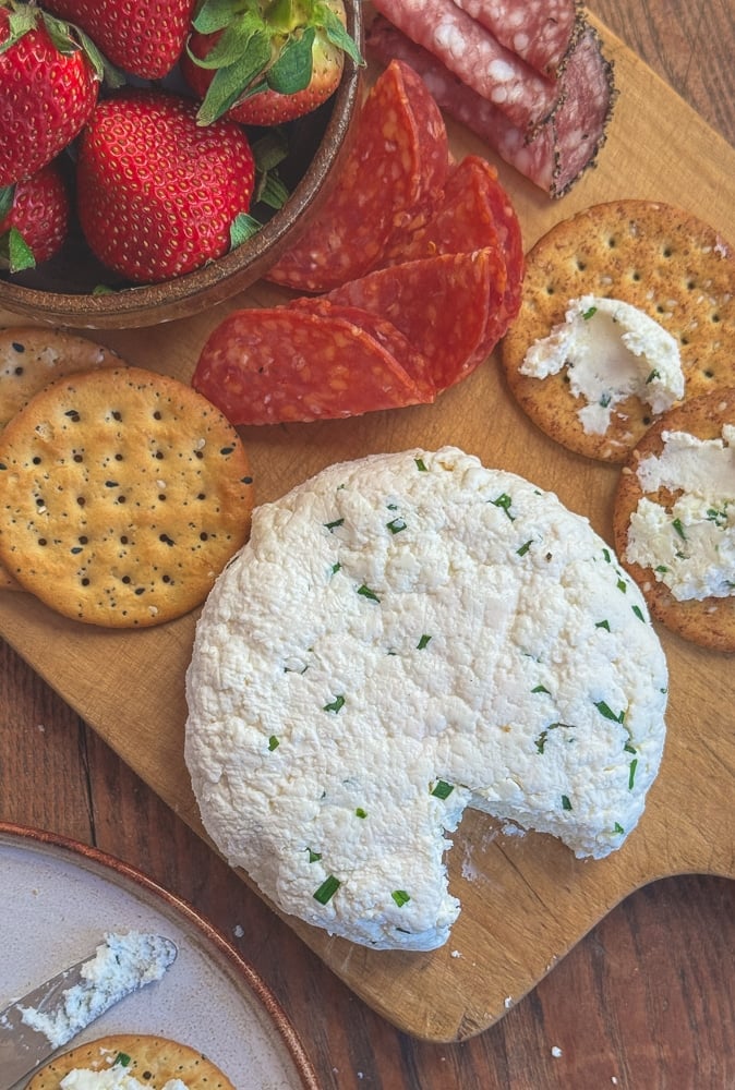 Overhead view of a charcuterie board with homemade chive farmers cheese, fresh strawberries, assorted crackers, and salami