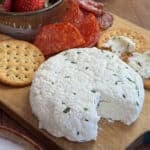 Rustic charcuterie board with a homemade herbed farmers cheese wheel, fresh strawberries, salami, crackers, and a glass milk bottle